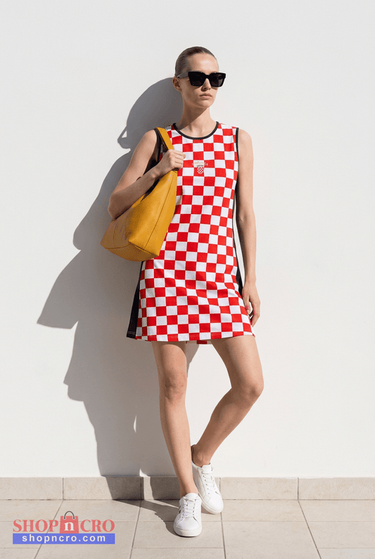 Dress Croatia Checks (shorter) Woman wearing a red and white checkered dress with sunglasses and a yellow bag against a white wall.