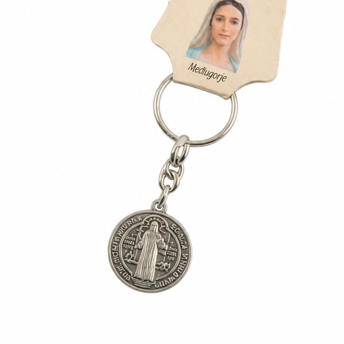 A silver-toned metal keychain featuring a round Medjugorje medal charm, attached to a white plastic key ring and a matching white plastic tag with a printed photo of Medjugorje. Međugorje Keyring Saint Benedict Medal in Silver