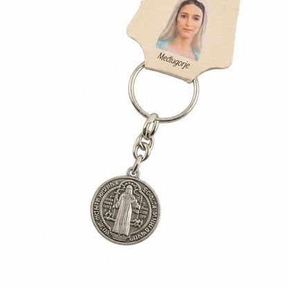 A silver-toned metal keychain featuring a round Medjugorje medal charm, attached to a white plastic key ring and a matching white plastic tag with a printed photo of Medjugorje. Međugorje Keyring Saint Benedict Medal in Silver
