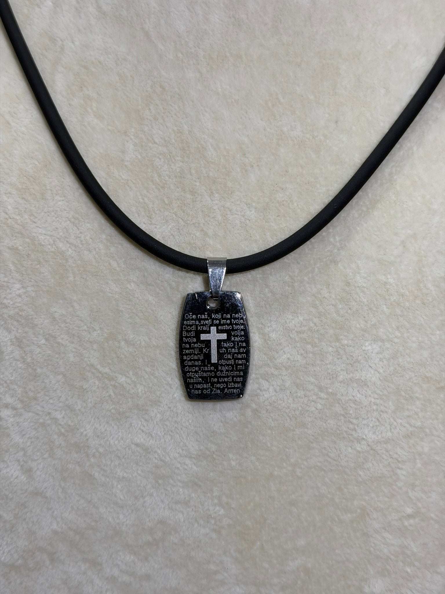 Oče Naš Necklace Black pendant with cross on a black cord against a light gray background