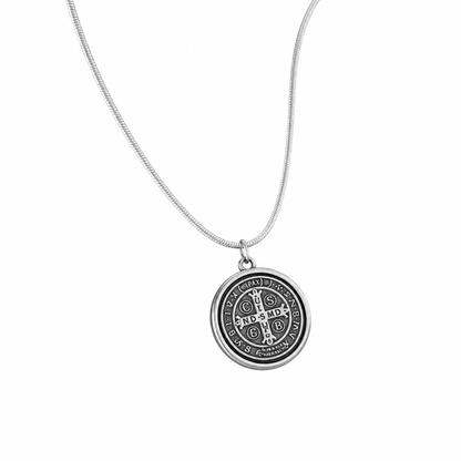 St. Benedict Medal | Pendant + Necklace or Pendant only A silver-toned Saint Benedict medal necklace featuring a circular pendant with an embossed monogram and text, suspended from a delicate snake chain against a plain white background.