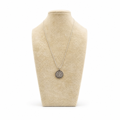 St. Benedict Medal | Pendant + Necklace or Pendant only A silver pendant necklace displayed on a beige fabric jewelry bust against a white background.