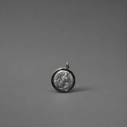 St. Benedict Medal | Pendant + Necklace or Pendant only A small round silver pendant or charm with an embossed figure and text, photographed on a smooth dark gray background.