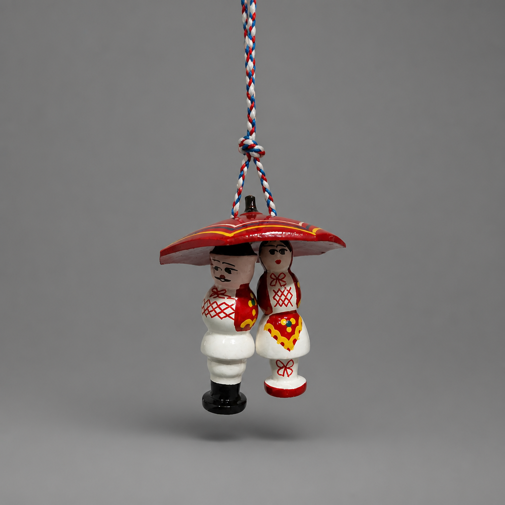 A traditional hand-painted wooden Polish ornament depicting a groom and bride under a red umbrella, suspended by a red, white, and blue braided string against a neutral gray background. Traditional Couple Under Šestine Umbrella Ornament