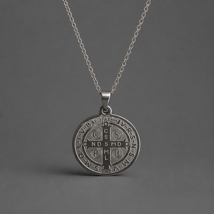 Croatian Medallion Necklace – St. Benedict Catholic Pendant A silver pendant necklace featuring an embossed circular Saint Benedict monogrammed cross pendant, suspended from a delicate silver chain against a dark gray background.